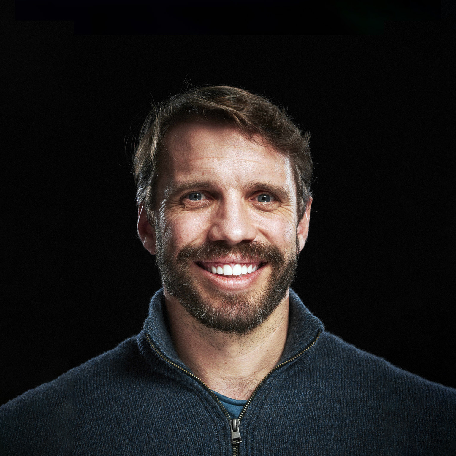 Ryan Petersen wearing a navy blue half-zip-collared sweater against a black studio backdrop.