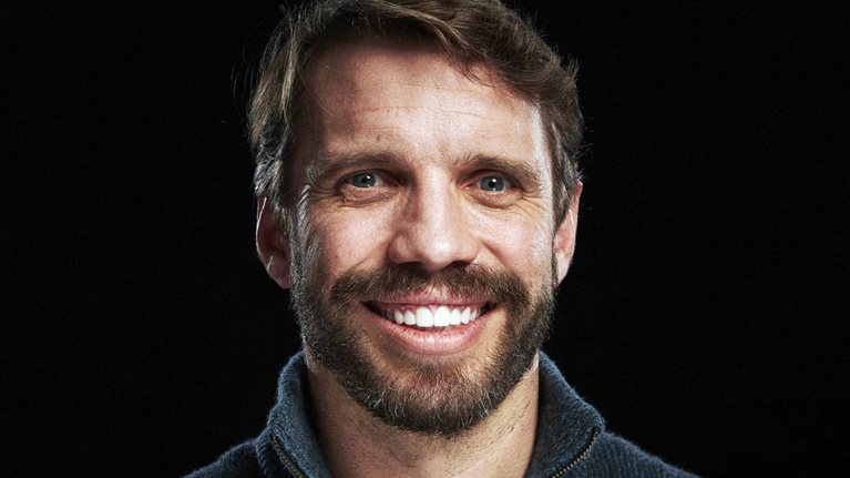 Ryan Petersen wearing a navy blue half-zip-collared sweater against a black studio backdrop.