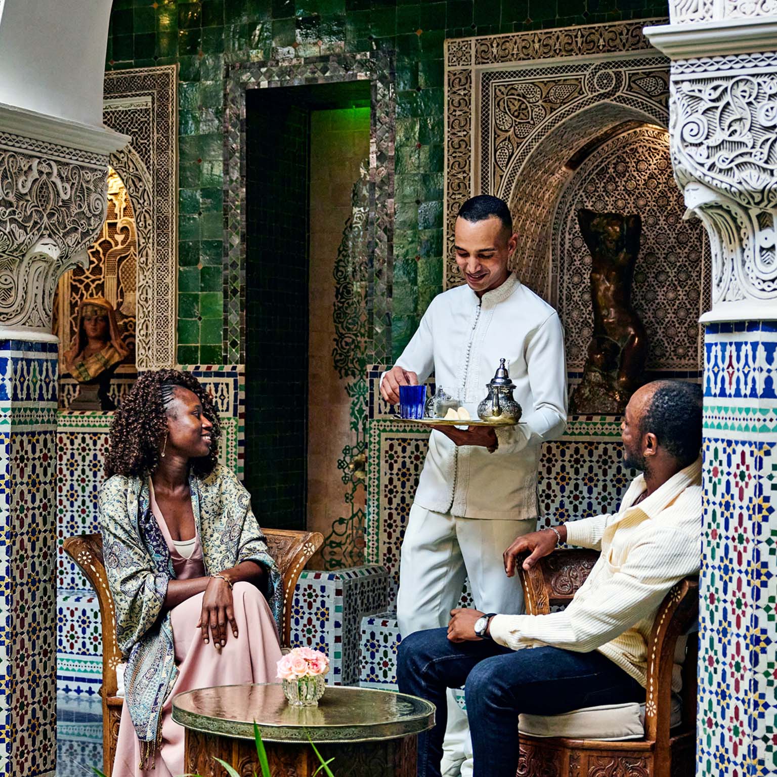 Smiling couple being served tea by concierge in courtyard of luxury hotel while on vacation