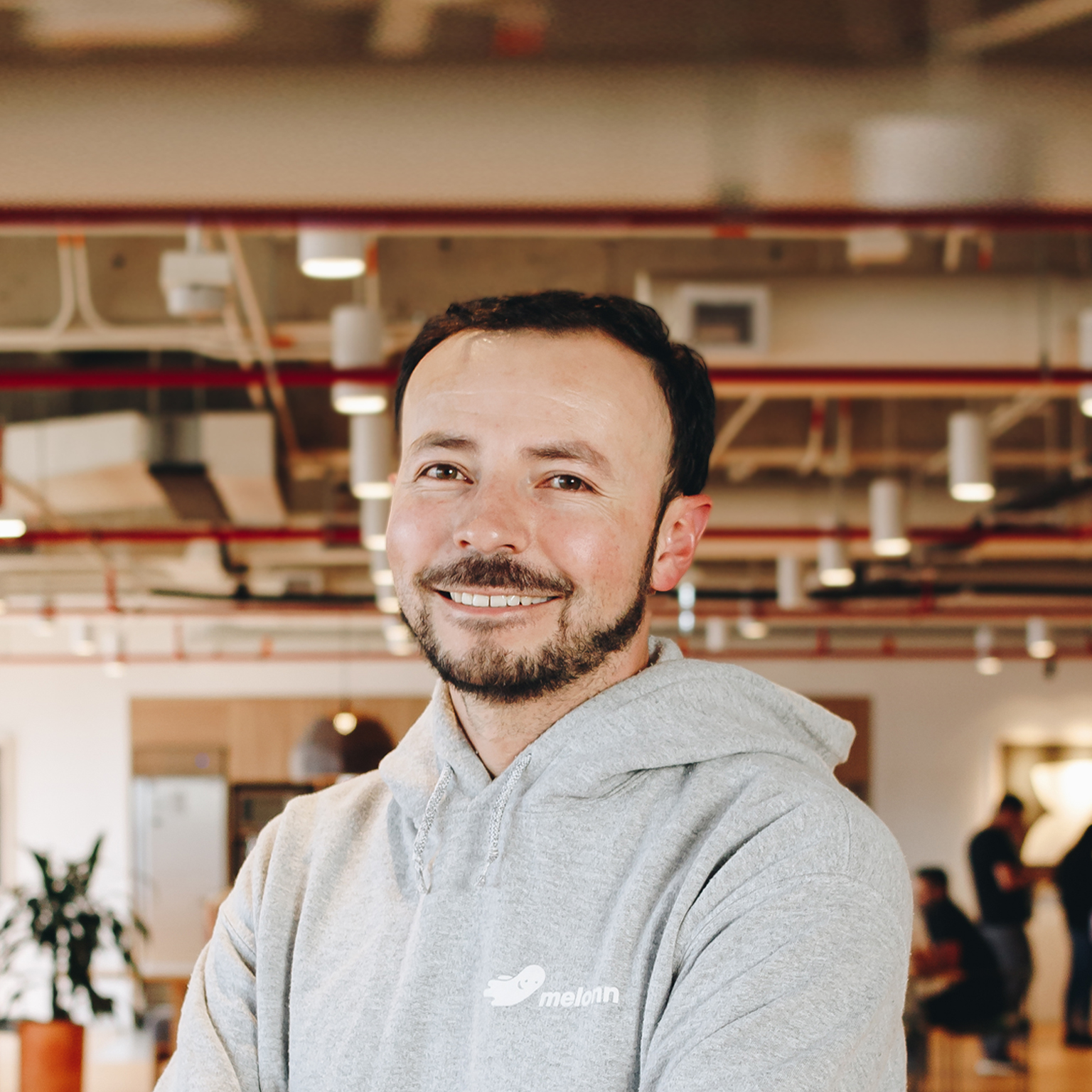 Portrait of a smiling Andres Melonn wearing a gray hoodie in a modern office. 
