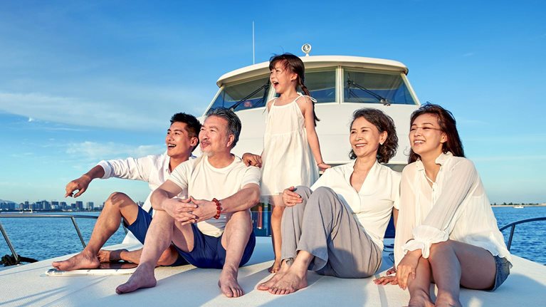 Image of an Chinese family cherishing the sunset while smiling and laughing, sitting on the front of a boat looking out to sea.