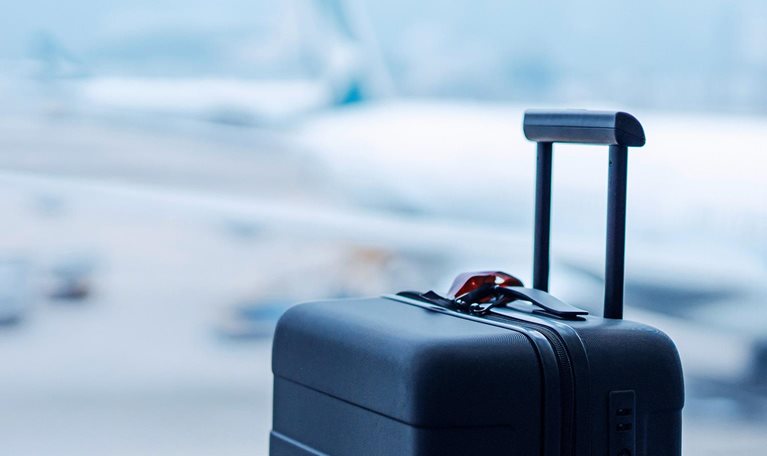A black suitcase in front of the window at international airport terminal, with blurred airplane in the background.