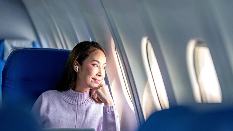 A woman passenger working mid-flight stops to gaze out her airplane window.