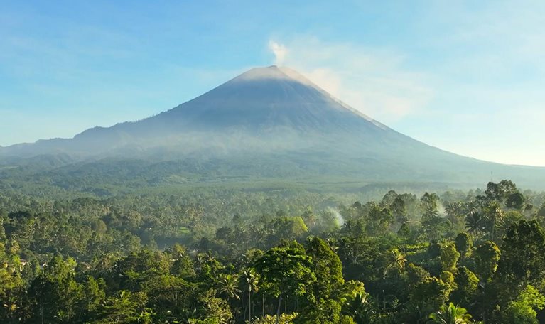 Scenic aerial view sunrise scene of Tumpak Sewu waterfall with Semeru Volcano Background with the jungles on Java Island, Indonesia.