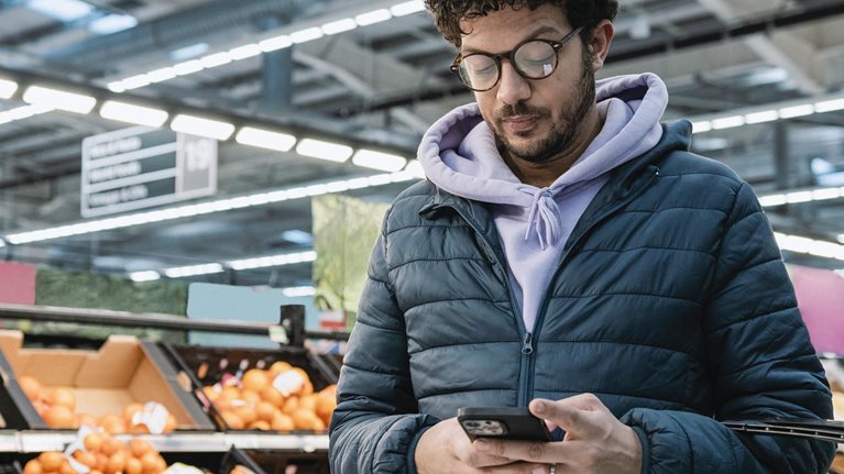 photo man in grocery store, holding shopping basket, looking at mobile phone