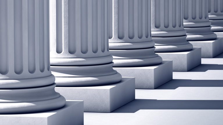 A deep row of stone columns with long linier shadows.