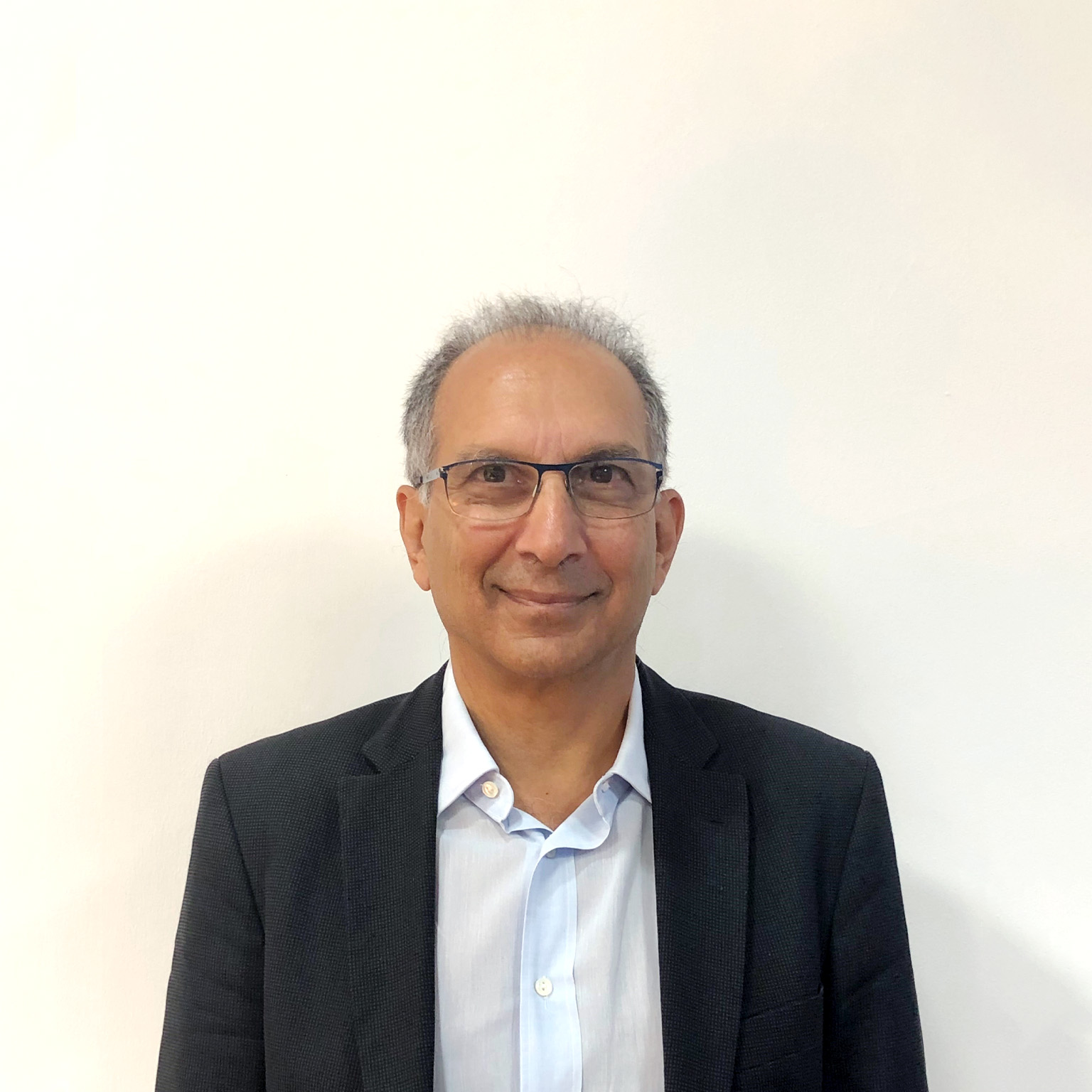 A smiling Homi Kharas photographed against a tan wall. 