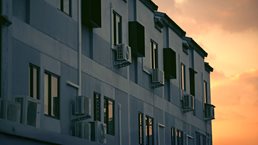 Image of an apartment building with air conditioning units next to the windows bathed in golden sunset.
