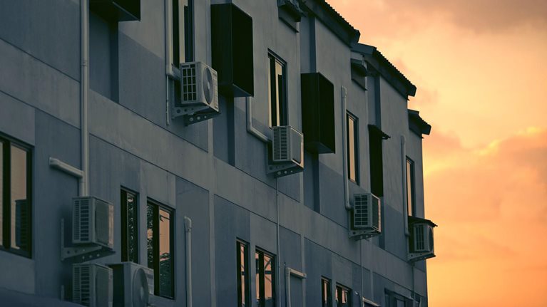 Image of an apartment building with air conditioning units next to the windows bathed in golden sunset.