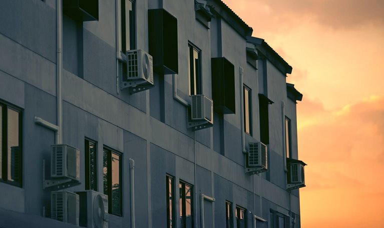 Image of an apartment building with air conditioning units next to the windows bathed in golden sunset.