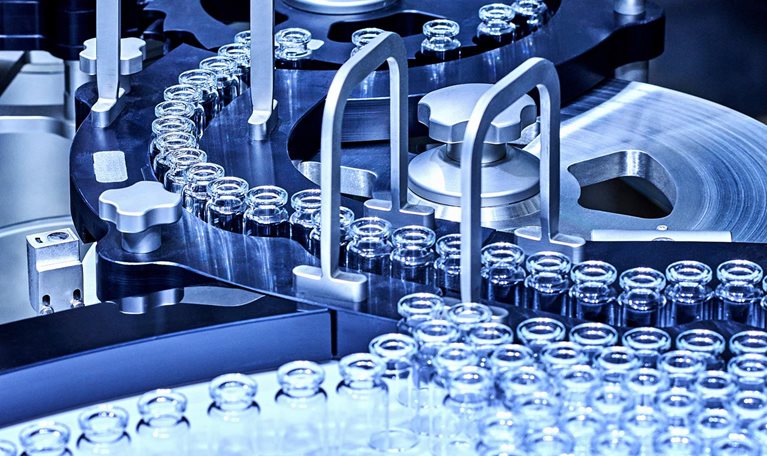 A pharmaceutical production line with rows of small glass vials moving through a complex stainless-steel machine.
