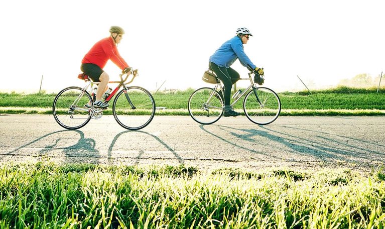 Wide shot of senior male friends on sunrise bike ride on rural road