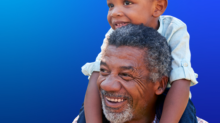 Grandfather carries grandson on shoulders during walk in park