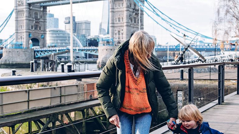Grandmother holding her grandson's hand while walking on a wooden walkway near the Tower Bridge in London, UK