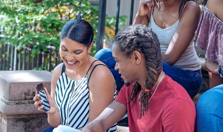 Group of Black friends together on the some stairs of a home, having fun looking at a mobile phone.